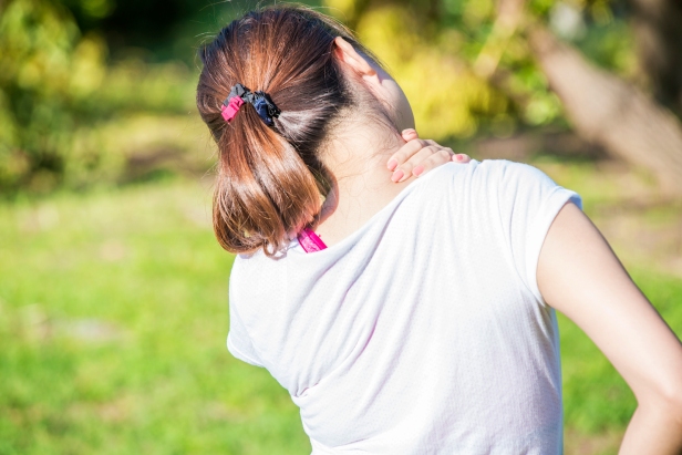 Back view of athletic young woman in sportswear touching her neck and lower back muscles by painful injury